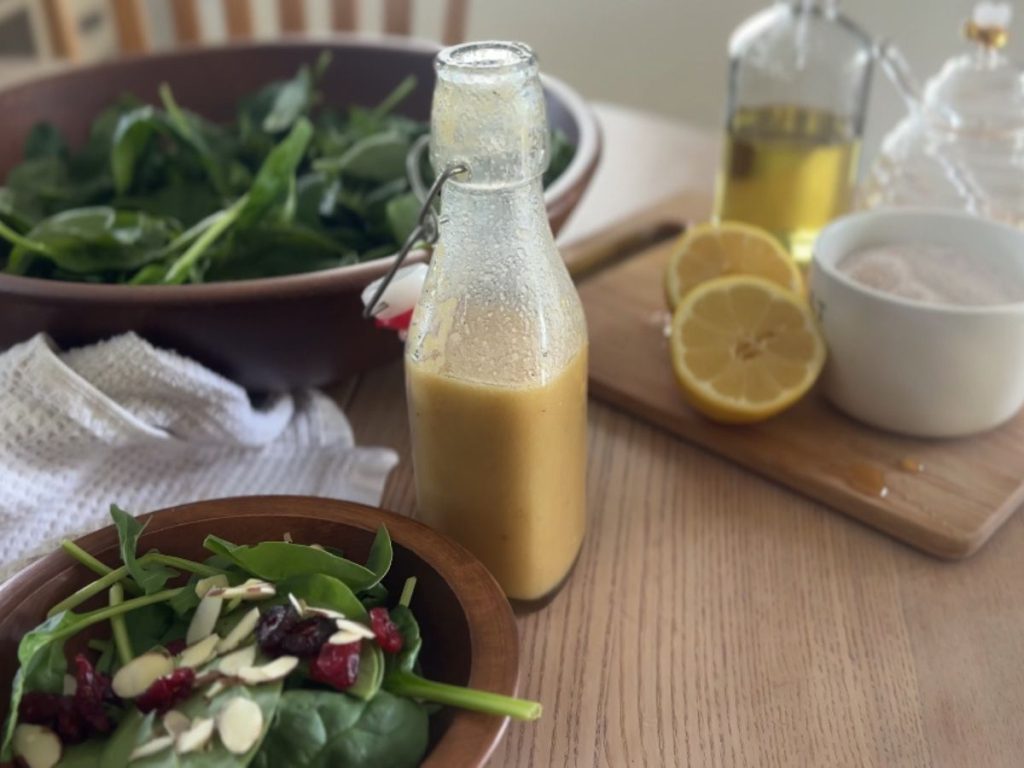 Salad greens next to a bottle of honey mustard vinaigrette and other ingredients used to make the dressing.