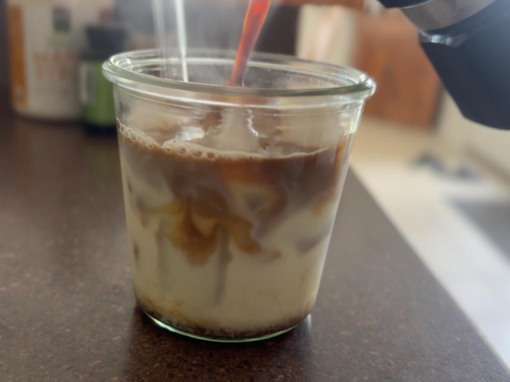 pouring espresso into a glass with milk and ice