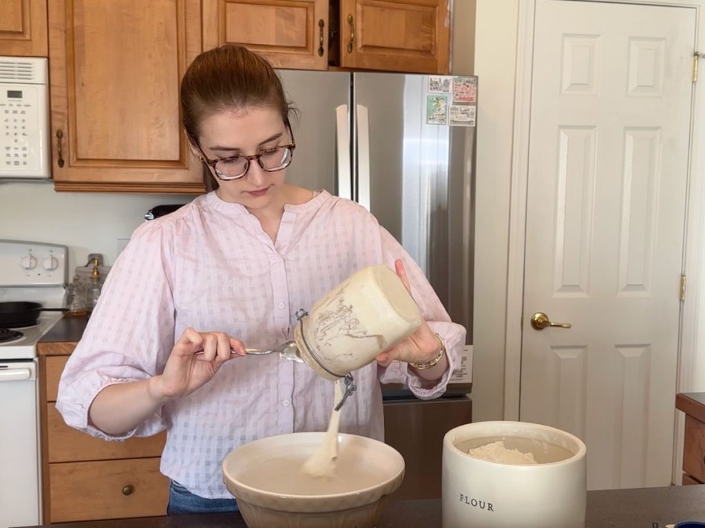 woman spooning sourdough starter into a bowl