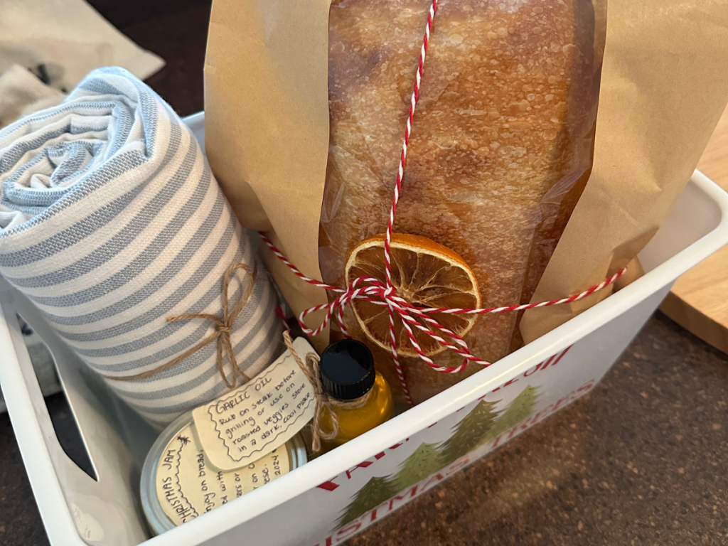 a basket full of homemade gifts including bread, jam, oil, and a kitchen towel